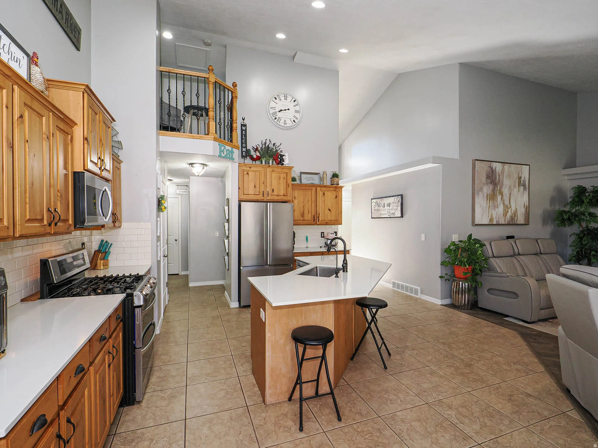 Open concept kitchen featuring wood cabinetry, stainless steel appliances, white subway tile backsplash, and a central island with a white countertop and integrated sink