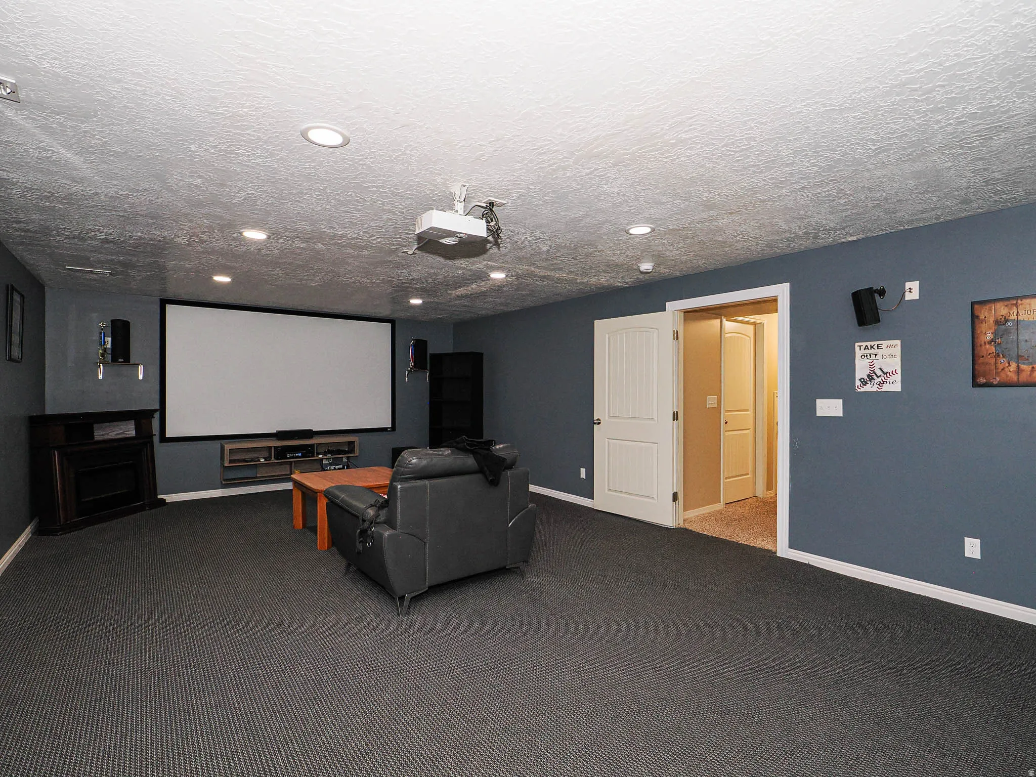 Dedicated media room featuring a large projection screen, recessed lighting, ceiling-mounted projector, and dark textured carpet