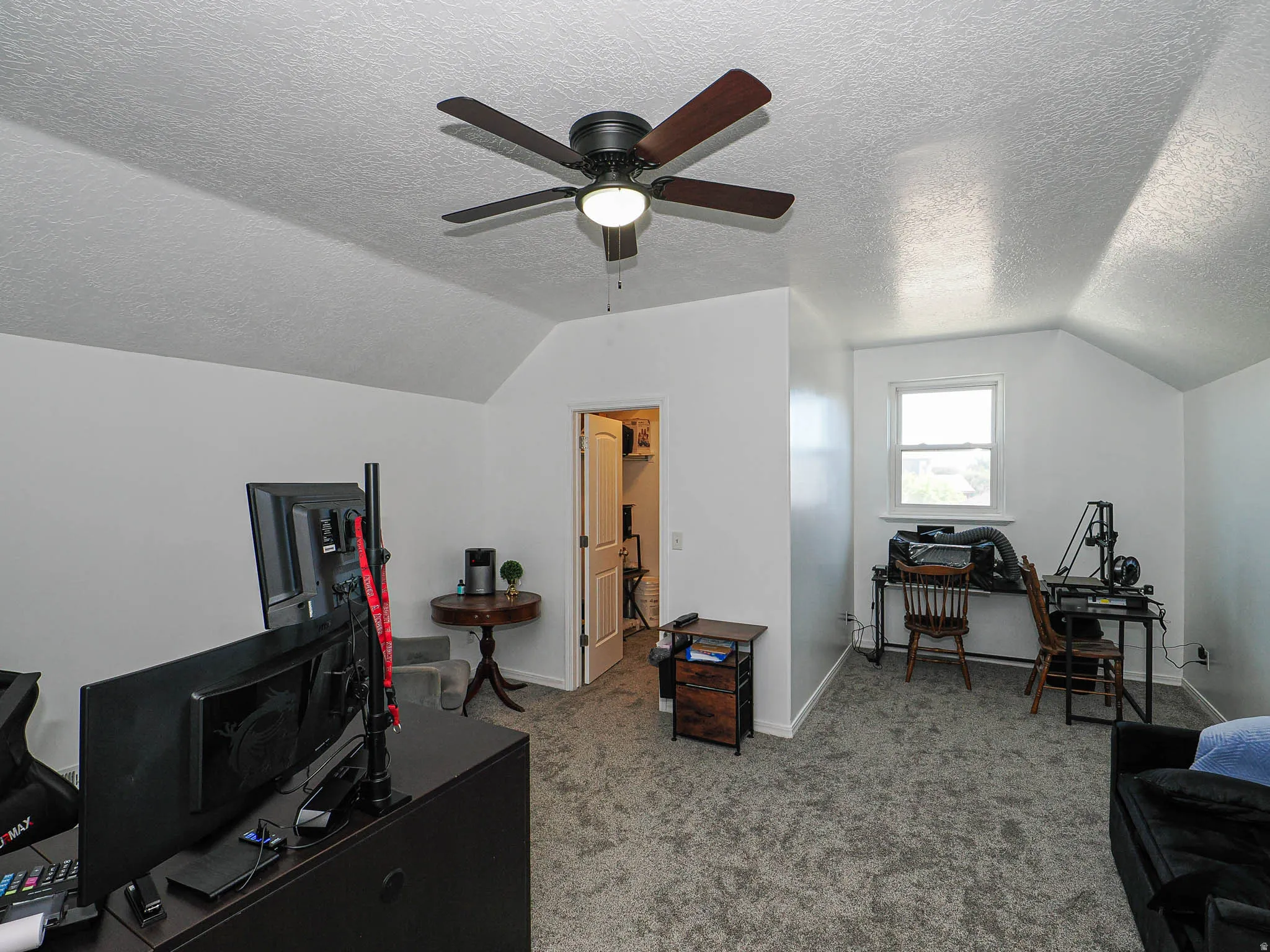Attic room featuring a ceiling fan with light, sloped ceilings, and gray carpet flooring