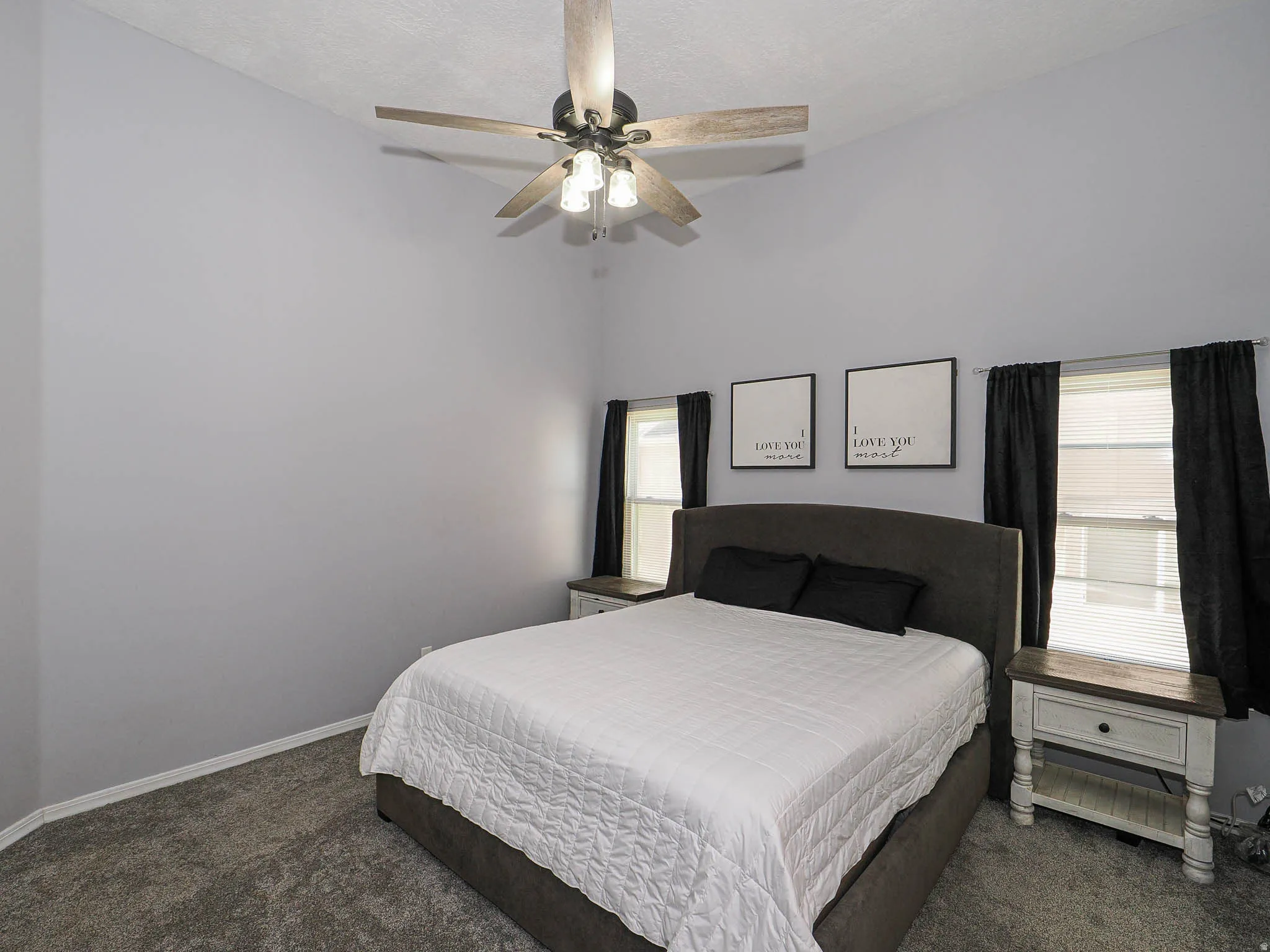 Vaulted ceiling bedroom featuring a ceiling fan with light fixture, dual windows with blinds, and gray carpet flooring