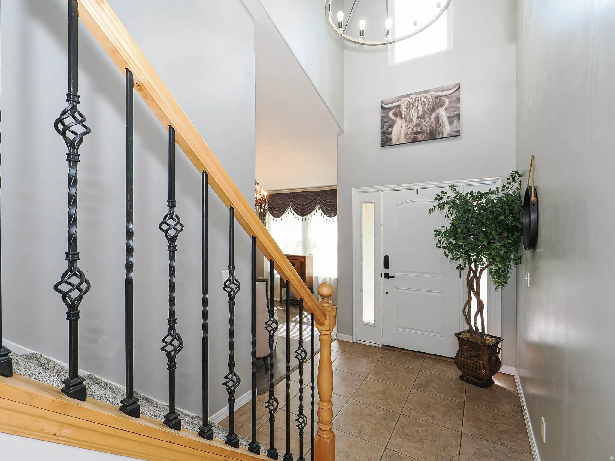 Two-story entryway featuring a light wood staircase with decorative wrought iron balusters, a large white entry door with a side light, and neutral tile flooring