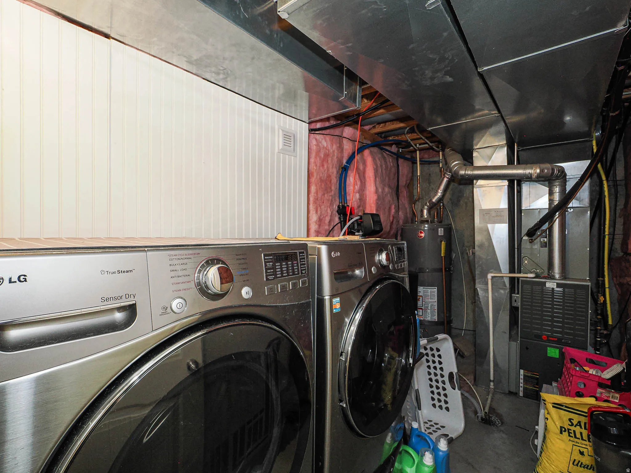 Laundry area featuring two stainless steel front-load appliances, exposed metal ductwork, and a water heater