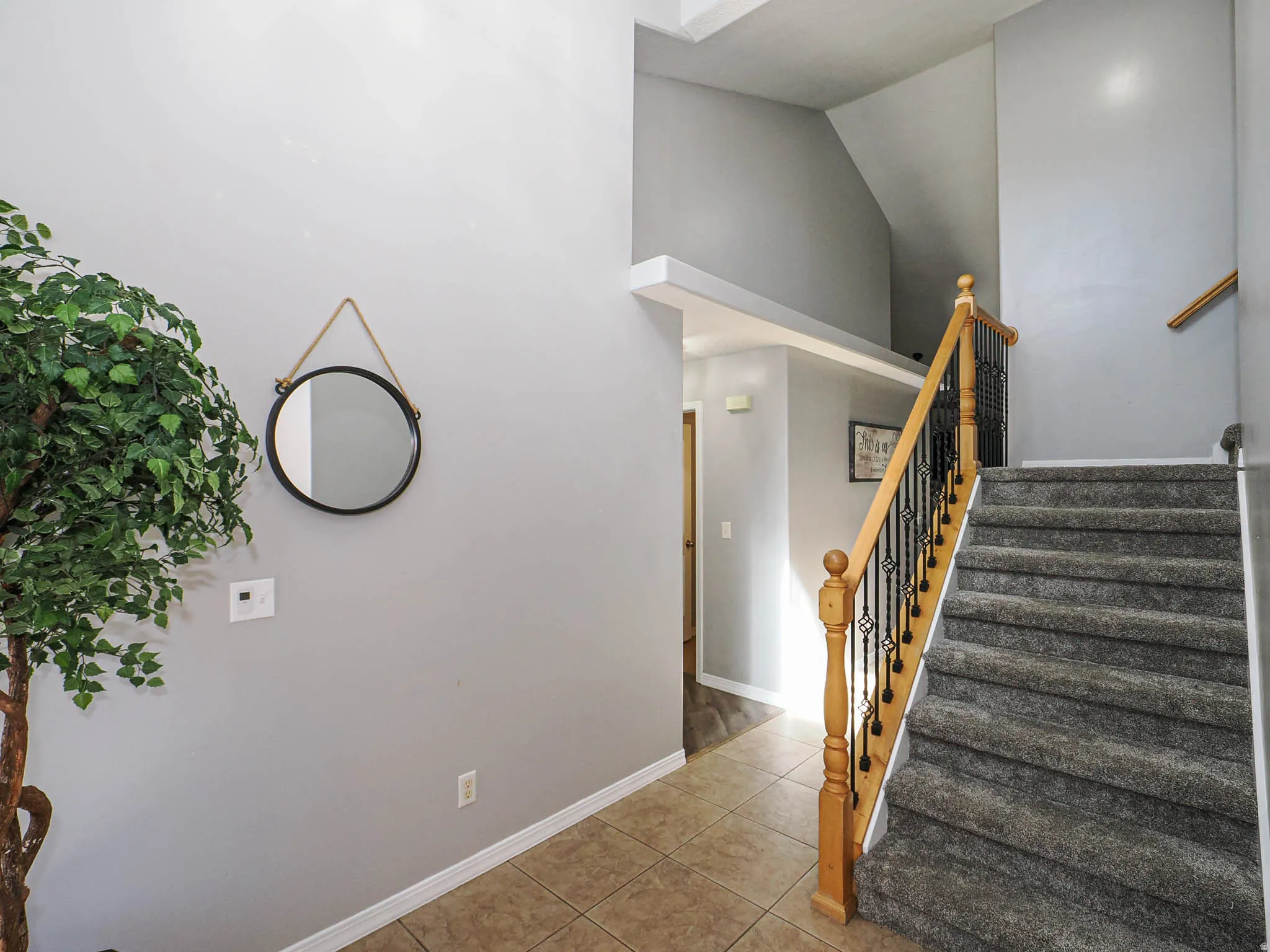 Entryway with high ceilings, carpeted staircase, wood banister, wrought iron balusters, and tile flooring