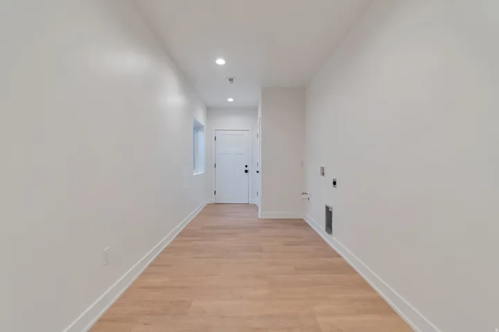 Long hallway featuring wood-finish flooring, white walls, recessed lighting, and a white paneled door