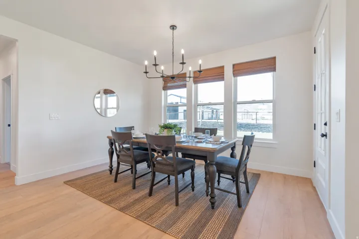 Dining area featuring a modern black chandelier, three windows with natural woven shades, light wood-finish flooring, and a white paneled door with a black handle