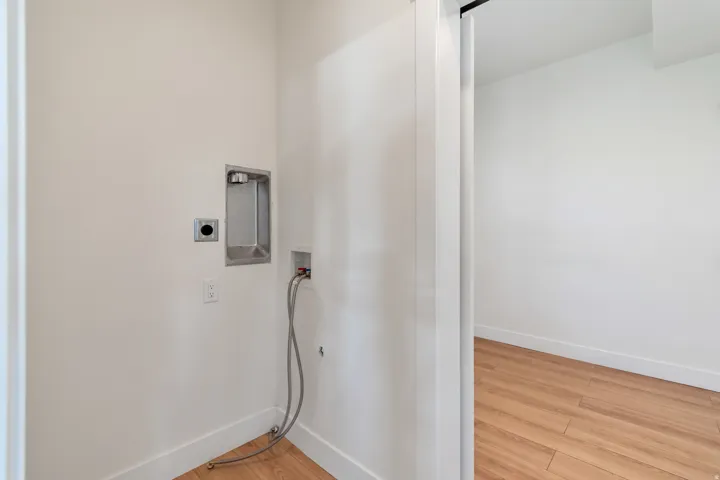 Dedicated laundry area featuring a white wall finish, white baseboards, and wood-finish flooring