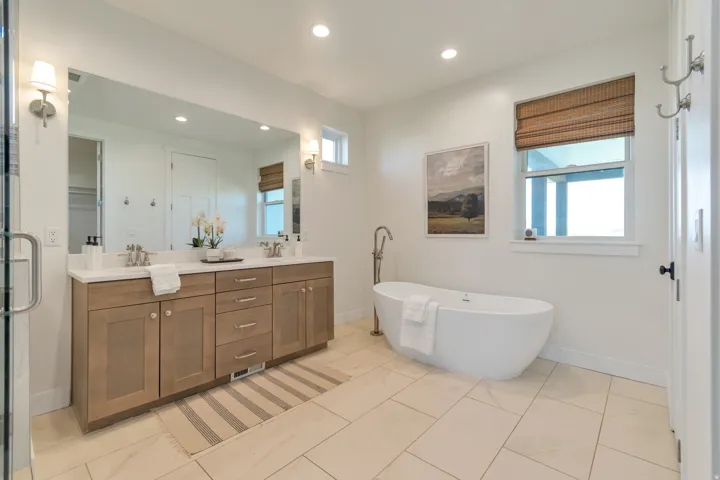 Spacious bathroom featuring a freestanding soaking tub, dual vanity with light-toned cabinetry, a large wall-mounted mirror, and tile flooring