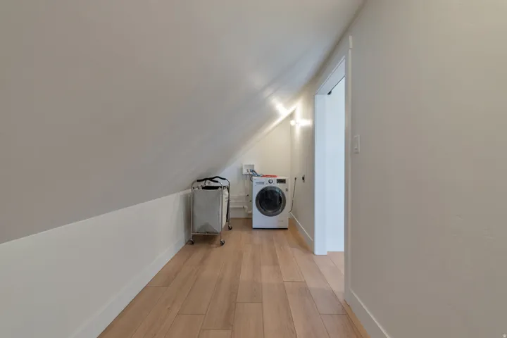 Dedicated laundry area featuring wood-finish flooring, white baseboards, and sloped ceilings