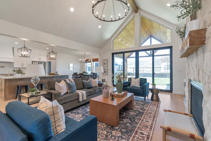 Vaulted ceiling with exposed beam, large-format sliding glass doors, white stone fireplace, and light wood-finish flooring