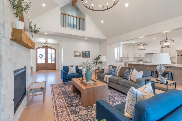Vaulted living space featuring a stone fireplace with a substantial wood mantel, light wood-finish flooring, and an overhead chandelier