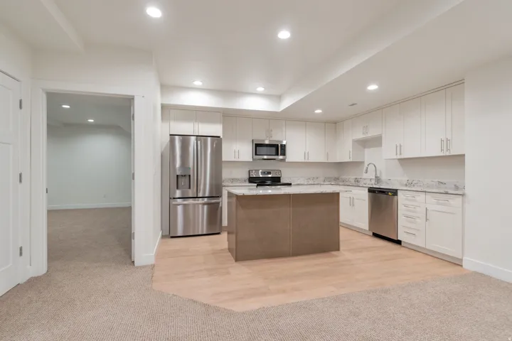 Kitchen featuring white cabinetry, stainless steel appliances, a center island with a contrasting base, light-toned countertops, and wood-finish flooring