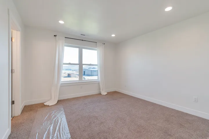 Spacious room featuring a large window, recessed lighting, neutral carpet flooring, white walls, and a white trim baseboard