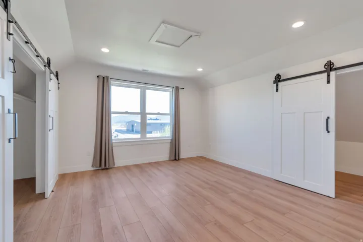 Spacious room featuring light wood-finish flooring, recessed lighting, and a window with neutral drapes