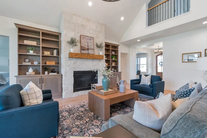 Spacious living area featuring a stone fireplace with a wood mantle, built-in shelving, vaulted ceilings, and wood-finish flooring