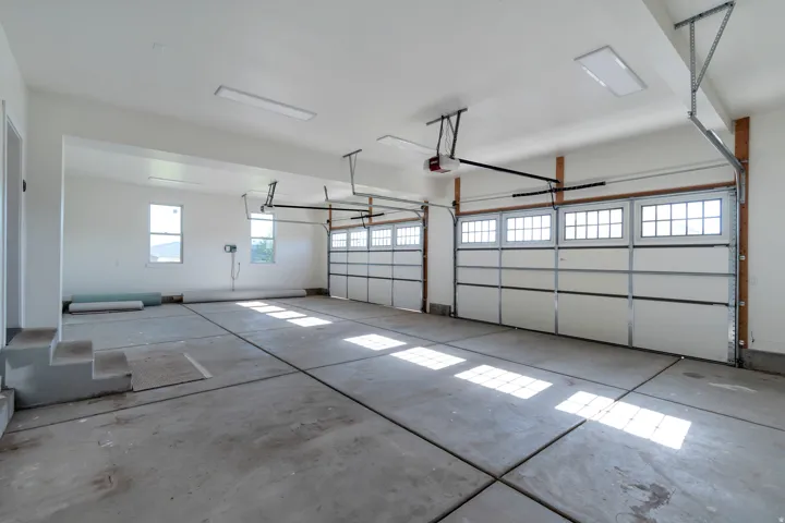 Spacious garage featuring concrete flooring, multiple windows, two garage door openers, and three overhead garage doors with upper window panels