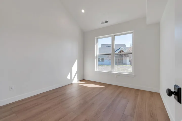 Room featuring wood-finish flooring, white walls, and a large window