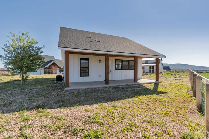 White vertical plank siding building featuring a dark shingle roof and a covered concrete patio