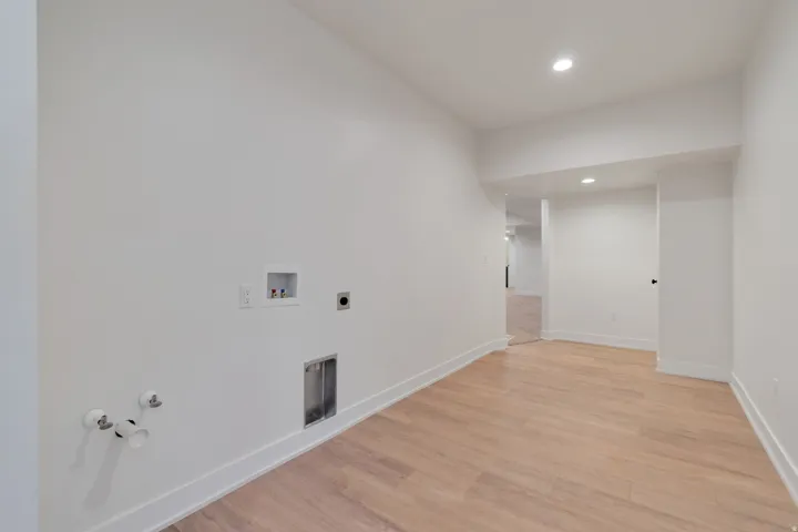 Spacious utility area featuring wood-finish flooring, recessed lighting, crisp white walls, white baseboards, and pre-installed laundry connections