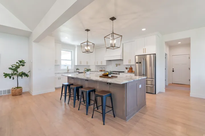 Expansive kitchen featuring a large central island with seating, white cabinetry, integrated stainless steel appliances, and wood-finish flooring