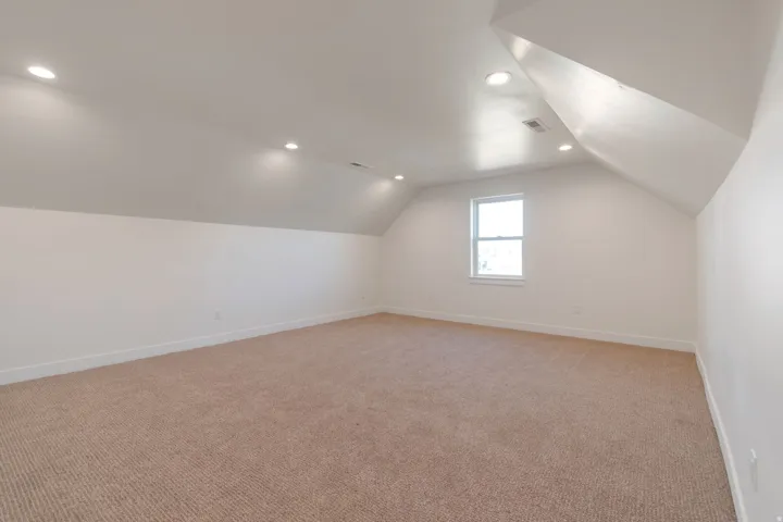 Spacious bonus room featuring an angled ceiling, recessed lighting, neutral carpeting, and a single window
