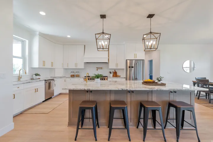 Open-concept kitchen featuring an oversized central island with seating, white shaker cabinetry, stainless steel appliances, and light wood-finish flooring