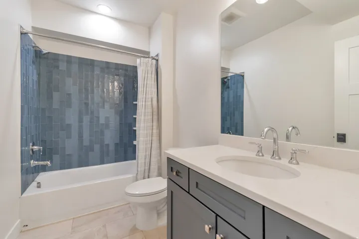 Bathroom featuring a tub/shower combination with blue vertical-set tile surround, a white vanity with an undermount sink, chrome fixtures, and a large mirror