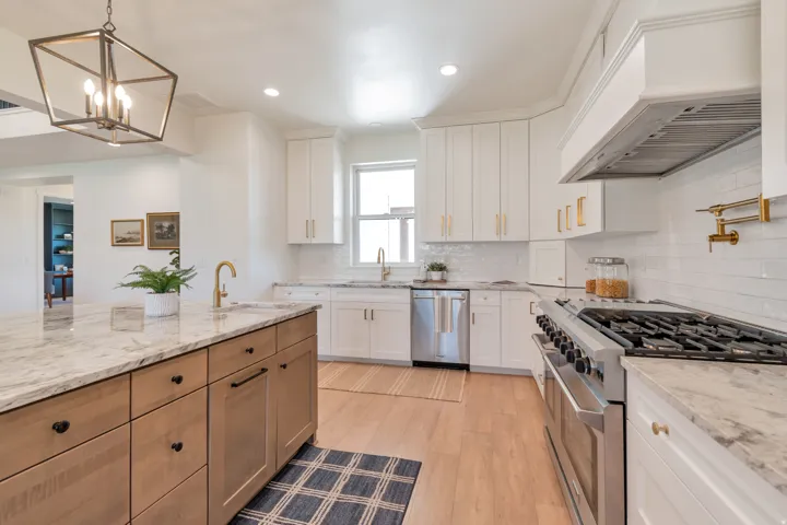 Gourmet kitchen with a large central island, light wood-finish flooring, white cabinetry, integrated stainless steel appliances, and a tiled backsplash