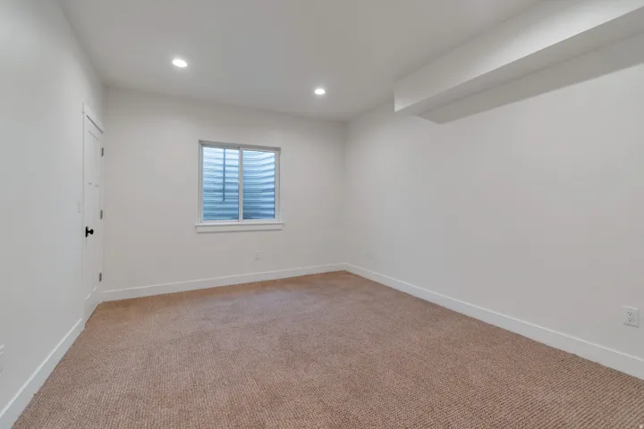 Carpeted room with recessed lighting, a white door with dark hardware, and a window with a window well
