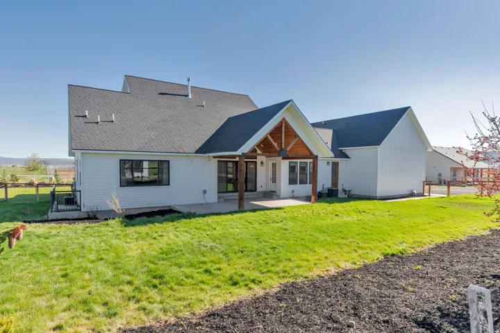Rear exterior showcasing a covered patio with exposed wood beams and columns, white siding, and black-framed windows