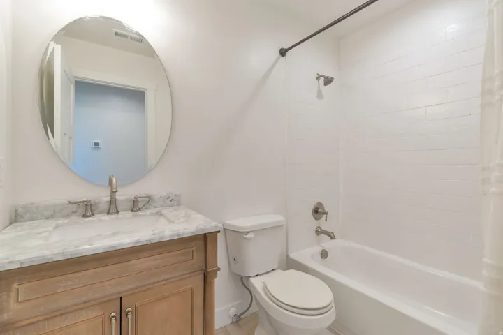 Bathroom featuring a light-toned wood vanity, stone countertop with integrated sink, and an oval mirror