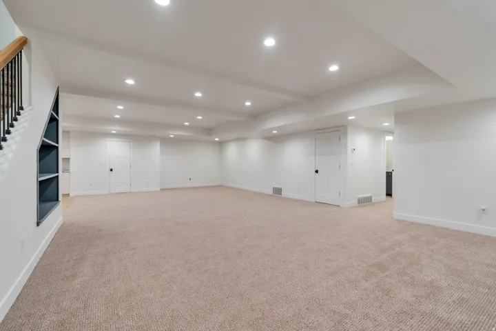 Spacious lower level featuring plush carpet flooring, recessed lighting, and a built-in shelving unit under the staircase