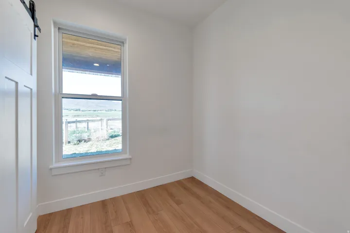 Bright interior space featuring wood-finish flooring, white walls, and a large window with a white frame