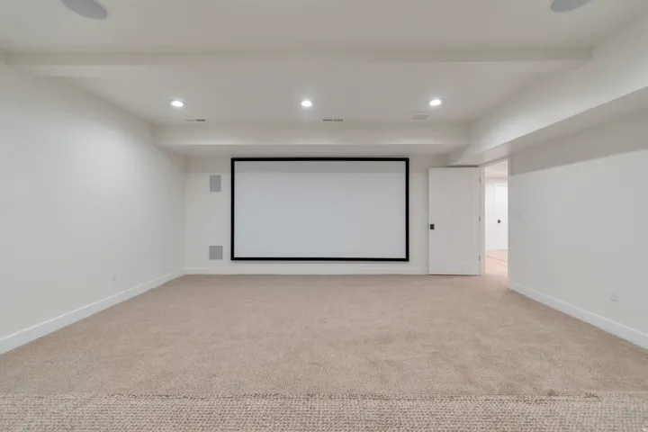 Spacious entertainment area featuring a large projection screen, integrated ceiling speakers, recessed lighting, and soft carpet flooring