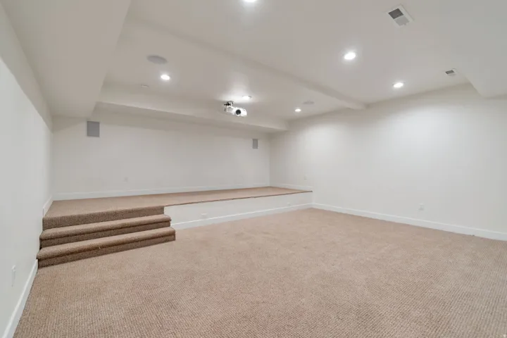Spacious multi-level room featuring plush carpeting, a built-in projector, recessed ceiling lighting, and integrated ceiling speakers