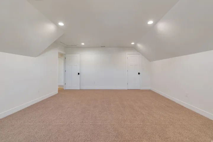 Spacious room featuring sloped ceilings, recessed lighting, neutral carpeting, crisp white walls, and two paneled doors with black hardware