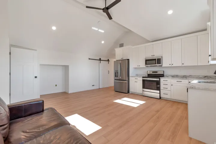 Modern kitchen and living area featuring wood-finish flooring, vaulted ceilings, and recessed lighting