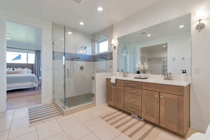 Spacious bathroom featuring a dual vanity with light wood cabinetry, a large frameless mirror, and a walk-in shower with glass enclosure