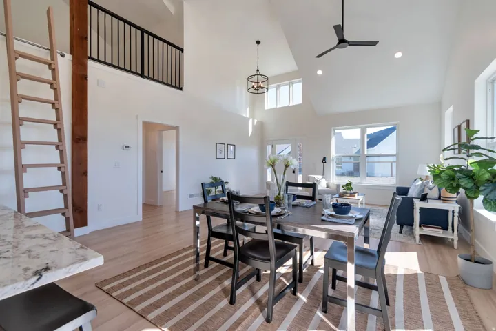 Open-concept living area featuring vaulted ceilings, light wood-finish flooring, and a second-story loft with a black metal railing