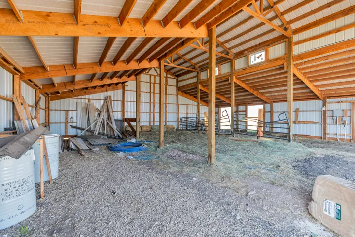 Spacious barn interior featuring exposed wood beams and posts, corrugated metal walls, a gravel and natural ground floor, and multiple open bays