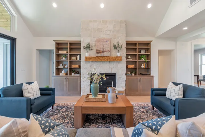 Living area featuring a stone-clad fireplace with a wood mantel, built-in shelving with lower cabinetry, vaulted ceilings, and recessed lighting
