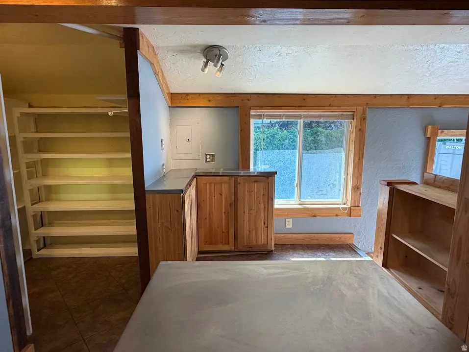 Wood-finish cabinetry with a light-colored countertop, recessed window with wood trim, built-in shelving, and exposed wood beams