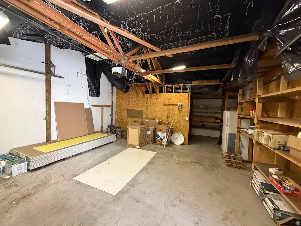 Spacious utility area featuring exposed wood ceiling beams, concrete flooring, and built-in shelving