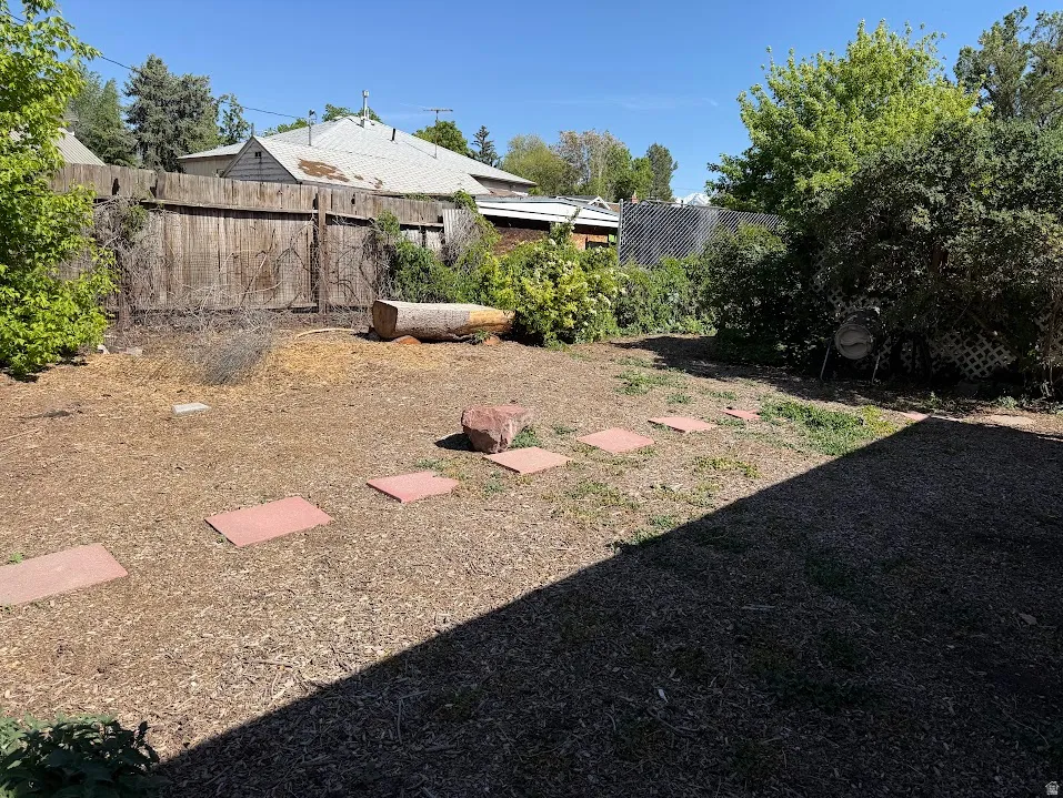 Expansive backyard featuring a wood chip ground cover, mature shrubs, a wooden privacy fence, and concrete paver stepping stones
