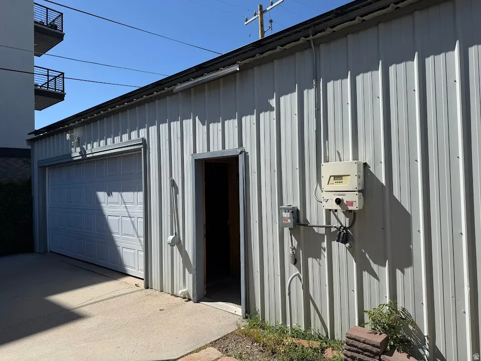 Corrugated metal exterior structure featuring a panel garage door, a pedestrian door, concrete paving, exterior electrical boxes, and a low-sloping roofline