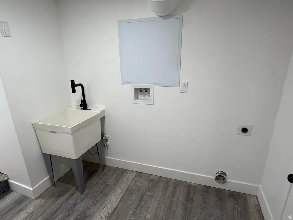 Dedicated laundry space featuring a utility sink with a matte black faucet, wall-mounted electrical outlets, and wood-finish flooring
