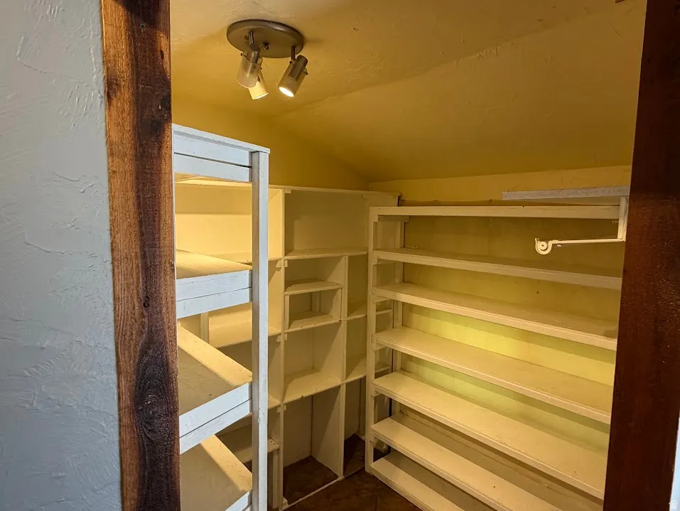 Walk-in storage area with extensive built-in shelving, track lighting, and a garment rod