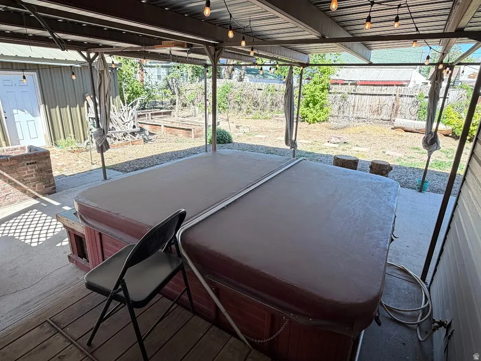 Covered patio area featuring a built-in spa with a cover, string lighting, and a corrugated metal roof