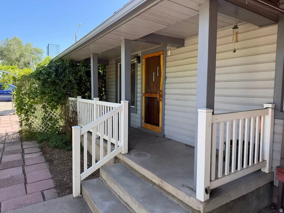 Front porch entry featuring a wood-finish screen door, light gray siding, and white railing