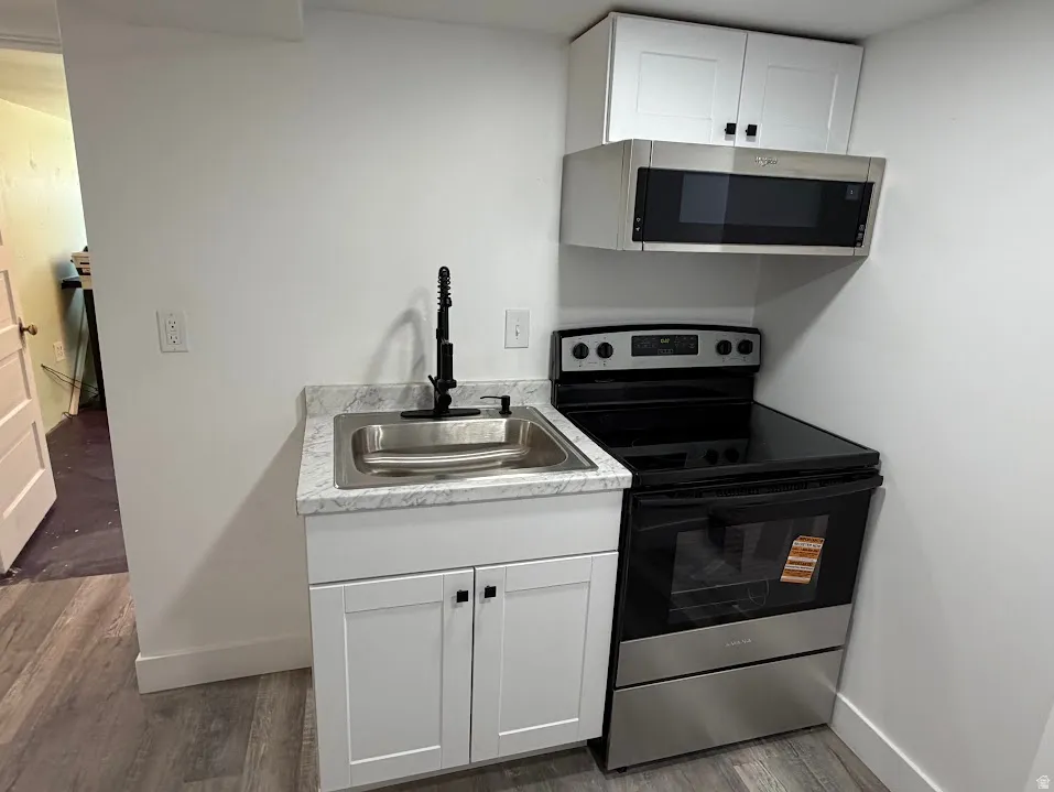 Compact kitchen area featuring a stainless steel sink with a matte black faucet, white shaker-style cabinetry, a stone-finish countertop, a stainless steel electric range, and an above-range microwave