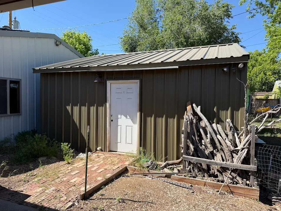 Corrugated metal storage shed featuring a metal roof and a white exterior door